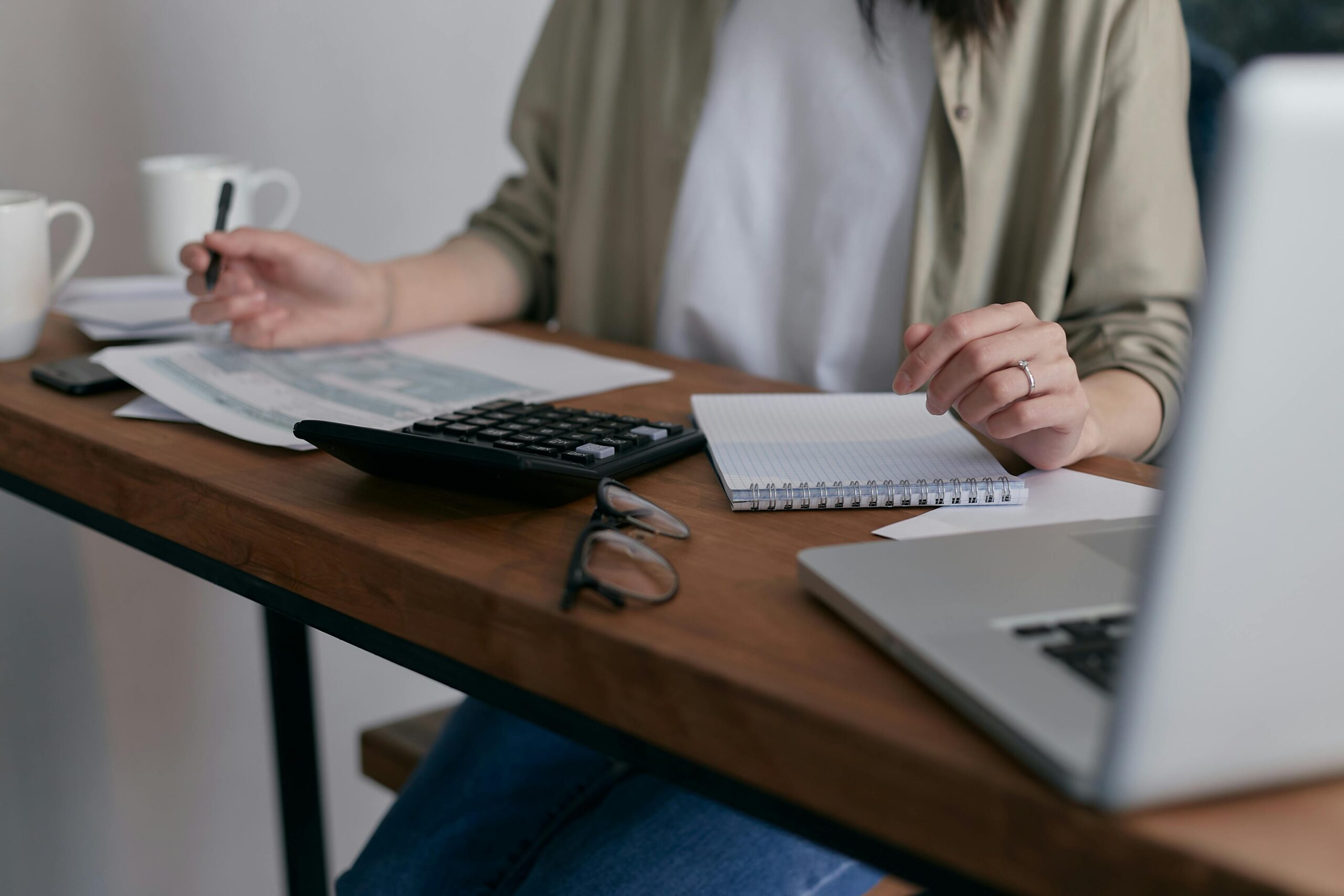 Image of a person sat at their desk, with documents, a laptop, and calculator open in front of them.